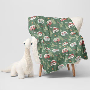 Christmas camper throw blanket with festive RV and pine tree print draped over chair.